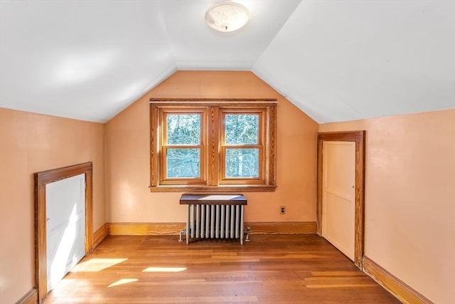 additional living space with vaulted ceiling, baseboards, light wood-style flooring, and radiator