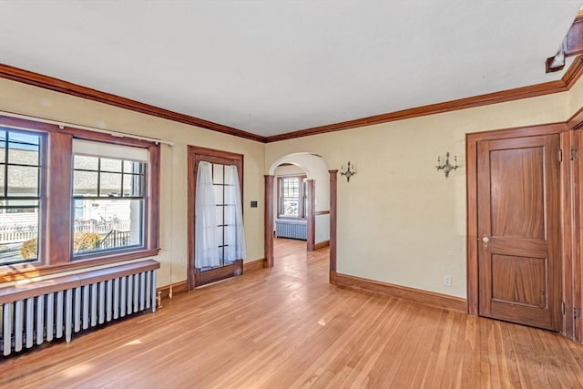 unfurnished room featuring light wood-type flooring, radiator heating unit, and arched walkways