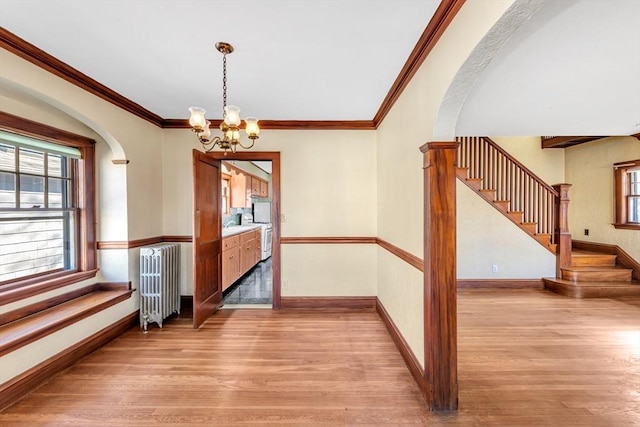 unfurnished dining area featuring arched walkways, stairs, light wood-style flooring, and radiator