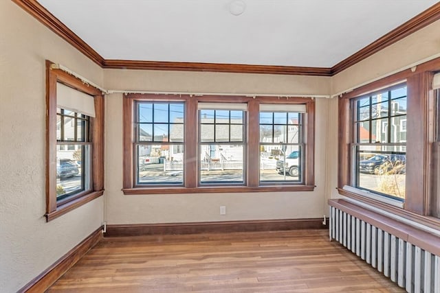 spare room featuring baseboards, light wood finished floors, radiator heating unit, and crown molding