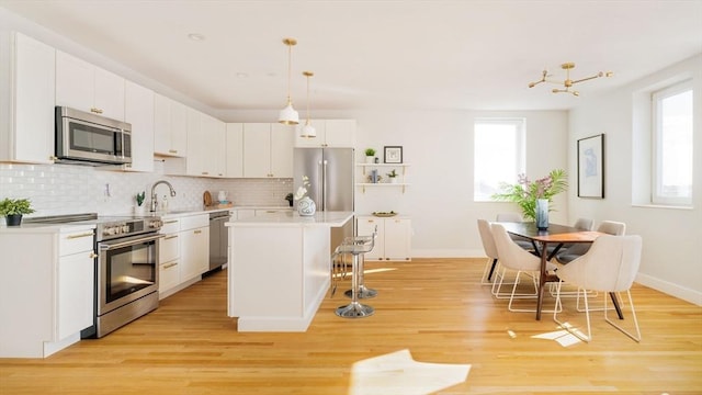 kitchen with appliances with stainless steel finishes, a kitchen island with sink, decorative backsplash, white cabinets, and decorative light fixtures