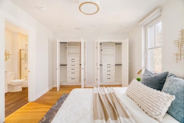 bedroom with two closets, ensuite bath, and light wood-type flooring