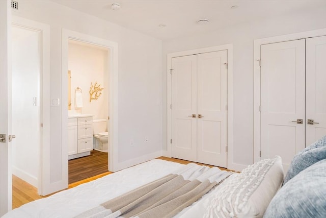 bedroom with multiple closets, ensuite bathroom, and light wood-type flooring