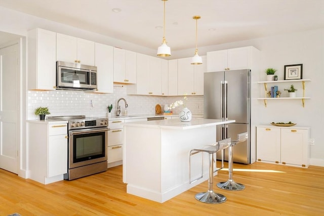 kitchen featuring sink, white cabinets, hanging light fixtures, stainless steel appliances, and light hardwood / wood-style flooring