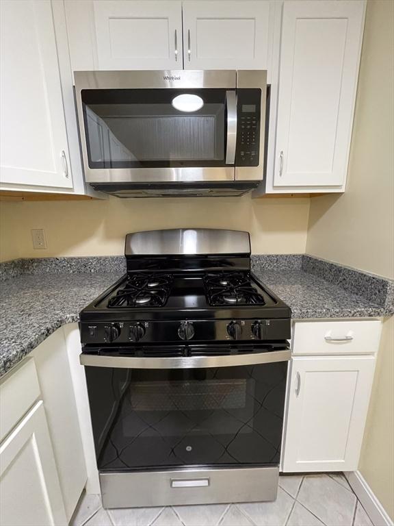 kitchen featuring gas stove, stone countertops, light tile patterned floors, and white cabinets