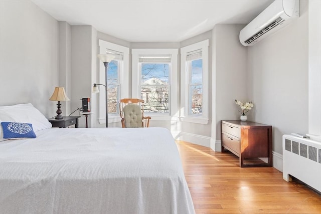 bedroom featuring baseboards, radiator heating unit, a wall mounted AC, and light wood-style floors