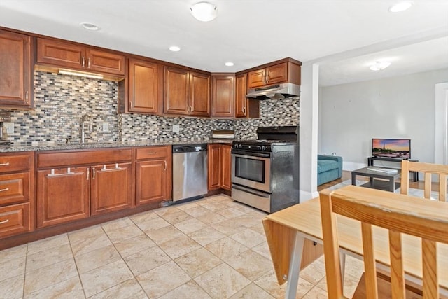 kitchen with under cabinet range hood, stainless steel appliances, a sink, brown cabinets, and tasteful backsplash