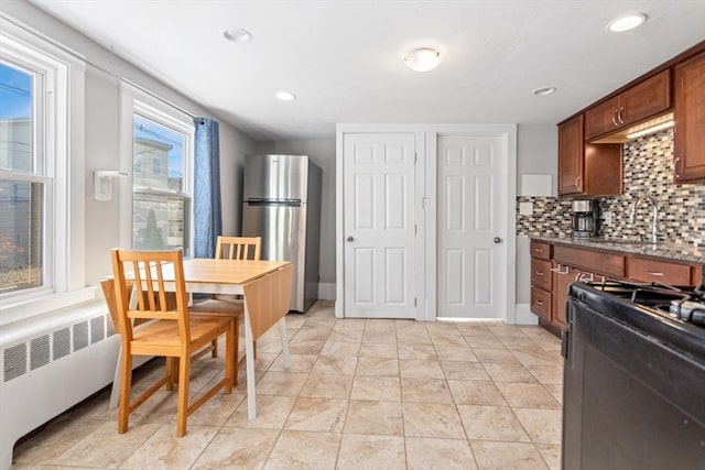 kitchen with range with gas cooktop, backsplash, radiator heating unit, stone countertops, and freestanding refrigerator