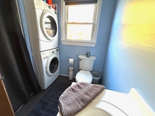 bathroom featuring toilet and stacked washer / dryer