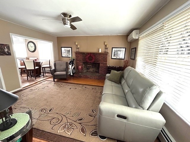 living room with baseboard heating, a wealth of natural light, wood-type flooring, and a wall mounted air conditioner