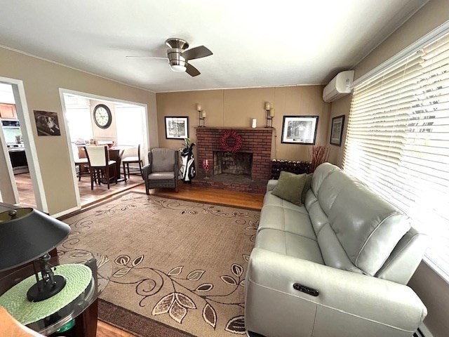 living room featuring a wall mounted AC, ceiling fan, wood-type flooring, crown molding, and a brick fireplace