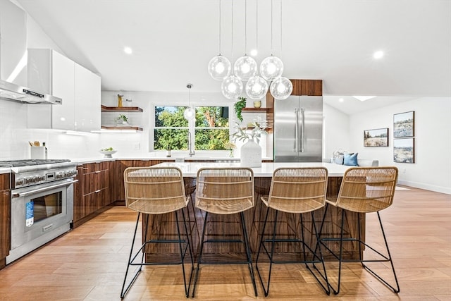 kitchen featuring white cabinets, a kitchen island, light hardwood / wood-style flooring, wall chimney range hood, and high quality appliances