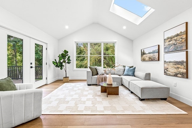 living room with vaulted ceiling with skylight, light hardwood / wood-style floors, and french doors