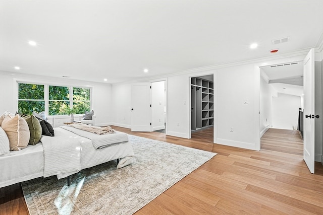 bedroom with light wood-type flooring, ornamental molding, a spacious closet, and a closet