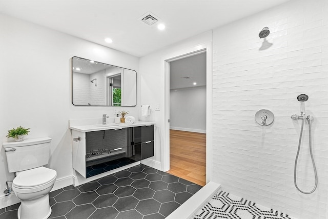 bathroom featuring vanity, hardwood / wood-style floors, a tile shower, and toilet