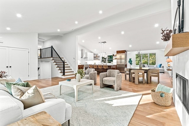 living room with light hardwood / wood-style floors, a fireplace, vaulted ceiling, and a notable chandelier