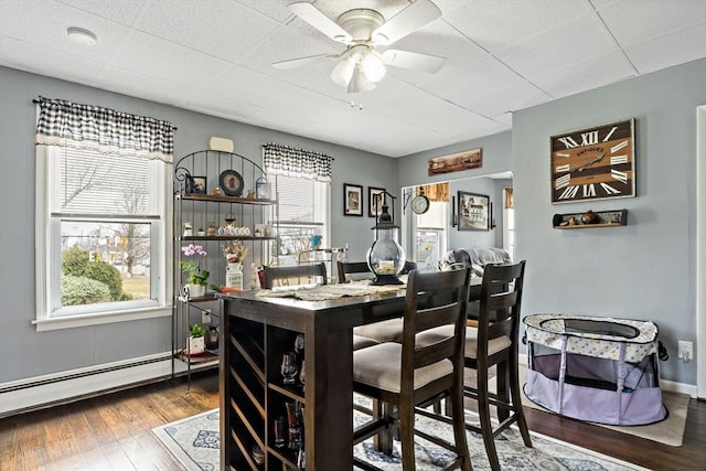 dining space featuring ceiling fan, a baseboard radiator, wood finished floors, and baseboards