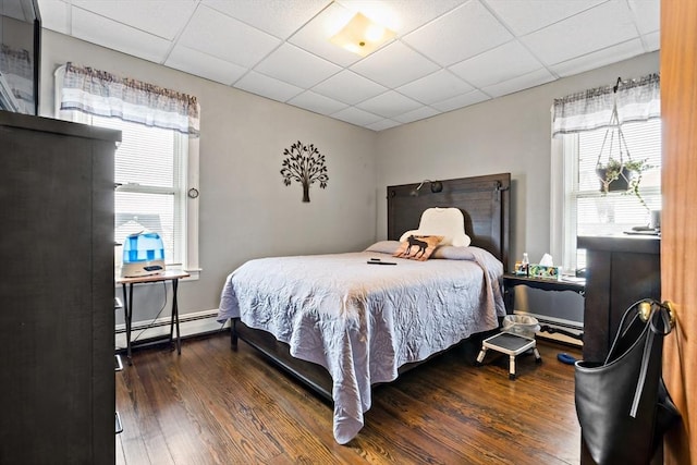 bedroom featuring baseboard heating, a drop ceiling, and wood finished floors