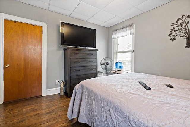 bedroom featuring a drop ceiling, wood finished floors, and baseboards