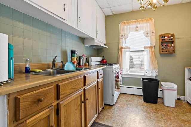 kitchen featuring white gas stove, a baseboard radiator, a sink, a drop ceiling, and under cabinet range hood