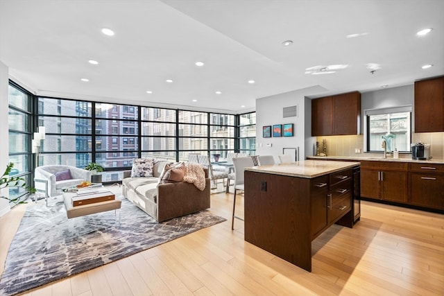 kitchen with backsplash, expansive windows, light hardwood / wood-style flooring, a kitchen island, and light stone counters