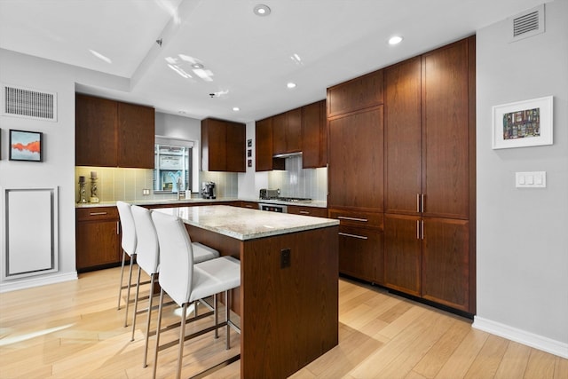 kitchen featuring a kitchen breakfast bar, a kitchen island, light hardwood / wood-style floors, and backsplash