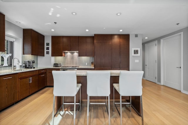 kitchen with a breakfast bar, a center island, light wood-type flooring, and sink