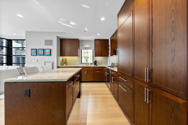 kitchen with sink, a kitchen island, tasteful backsplash, light hardwood / wood-style floors, and a kitchen bar