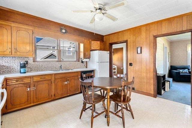 kitchen featuring sink, white refrigerator, wooden walls, ceiling fan, and backsplash