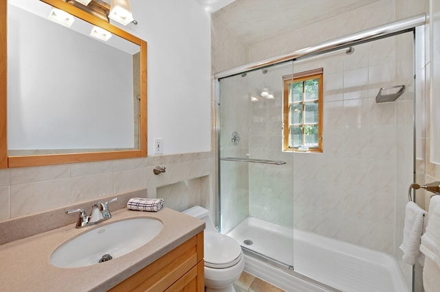 bathroom featuring tile walls, vanity, toilet, and a shower with door