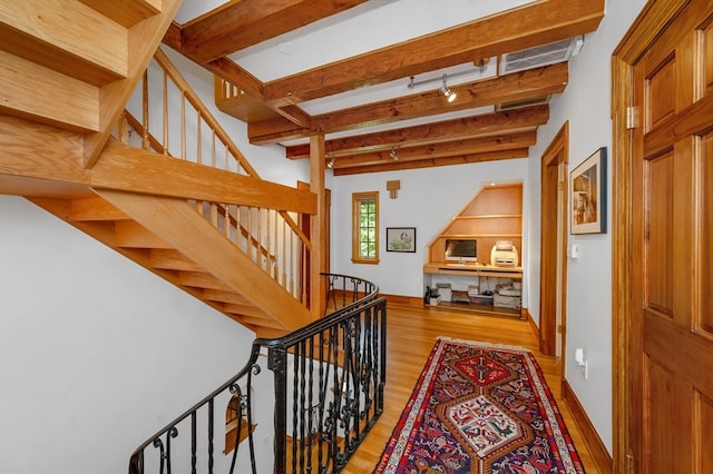 stairs with beam ceiling, track lighting, and hardwood / wood-style floors