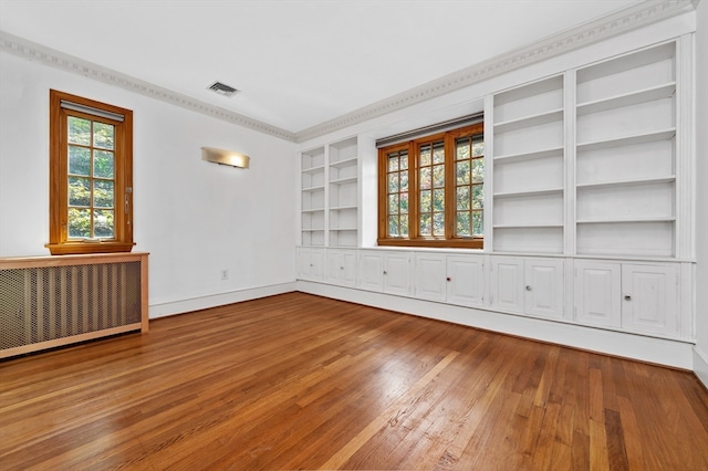 empty room with ornamental molding, built in shelves, radiator, and hardwood / wood-style flooring