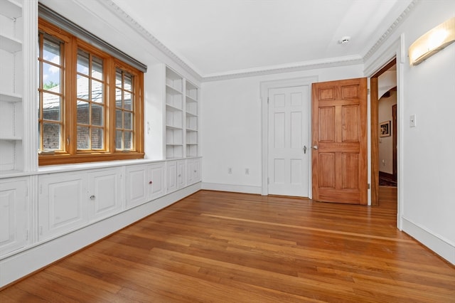 unfurnished room featuring built in shelves, hardwood / wood-style flooring, and crown molding