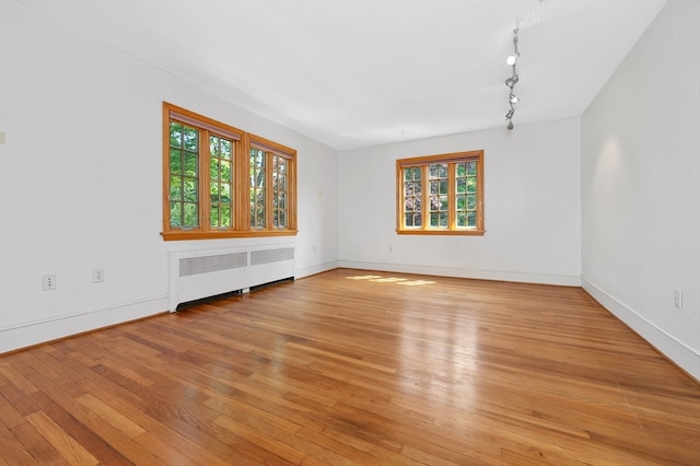 unfurnished room with track lighting, light hardwood / wood-style floors, radiator heating unit, and a healthy amount of sunlight