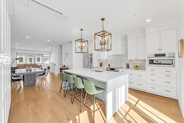 kitchen with white cabinets, open floor plan, light countertops, appliances with stainless steel finishes, and an island with sink