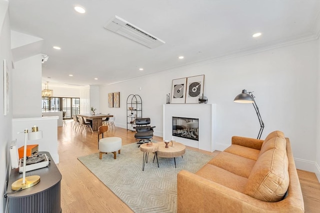 living room featuring recessed lighting, baseboards, light wood-style floors, ornamental molding, and a glass covered fireplace