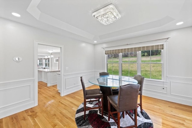 dining area with a tray ceiling, a chandelier, light wood finished floors, and a decorative wall