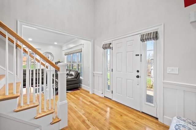 foyer entrance featuring crown molding, a decorative wall, a wainscoted wall, wood finished floors, and stairway