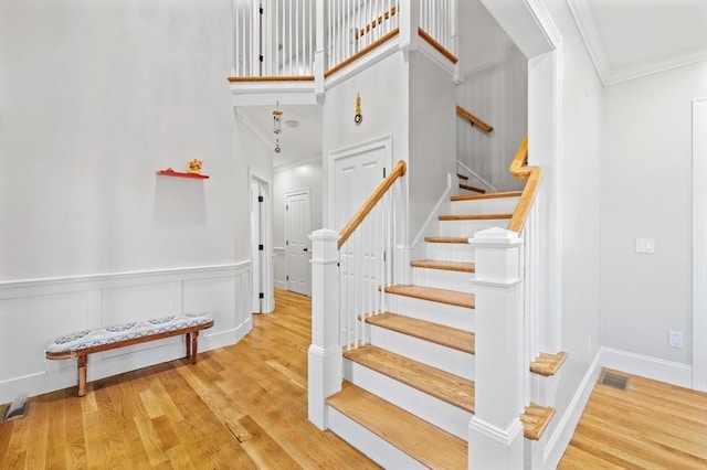 stairs with a towering ceiling, ornamental molding, wood finished floors, and visible vents