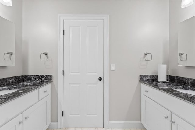 bathroom with baseboards, a sink, and two vanities
