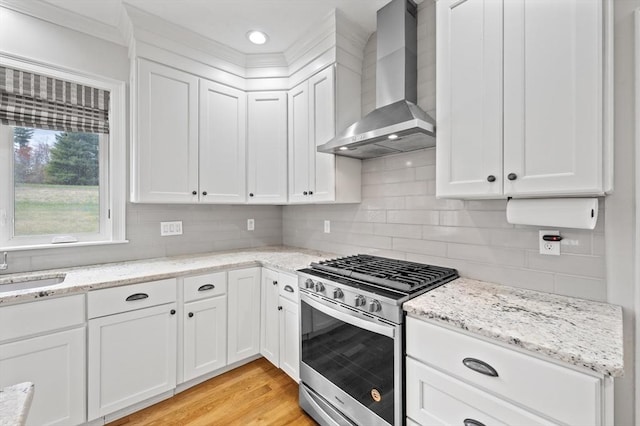 kitchen with white cabinets, light wood finished floors, stainless steel range with gas cooktop, and wall chimney exhaust hood