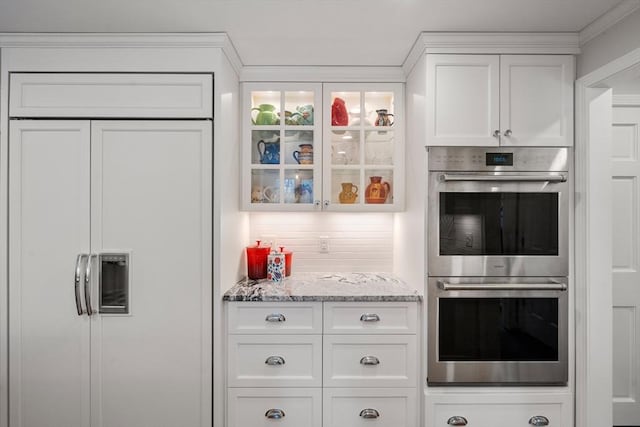 kitchen with tasteful backsplash, glass insert cabinets, paneled refrigerator, stainless steel double oven, and white cabinetry