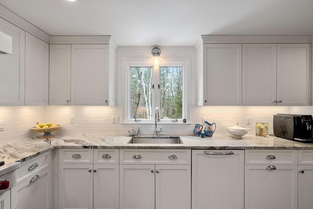 kitchen featuring light stone counters, tasteful backsplash, a sink, and white cabinetry