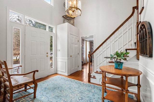 foyer entrance with light wood finished floors, a towering ceiling, a wainscoted wall, stairway, and a chandelier