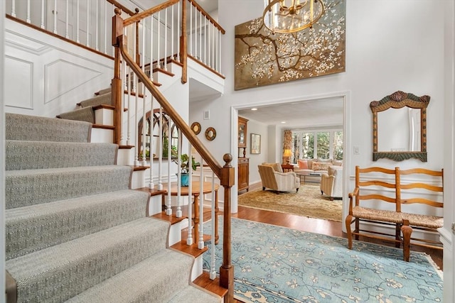 staircase with a towering ceiling, a notable chandelier, baseboards, and wood finished floors