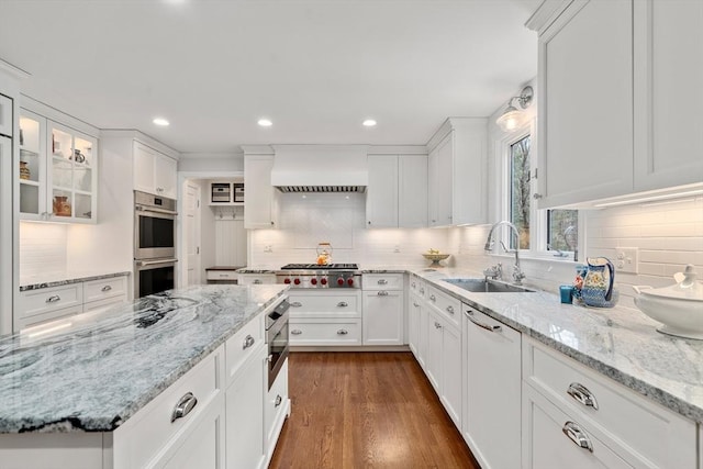 kitchen with double oven, custom range hood, white cabinetry, and a sink