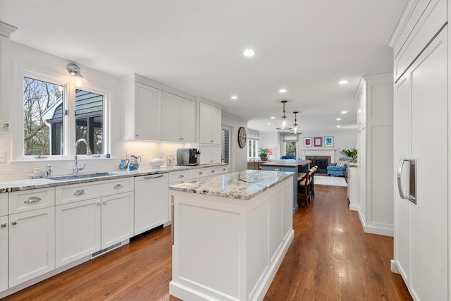 kitchen with decorative backsplash, white cabinets, a kitchen island, a sink, and dishwasher