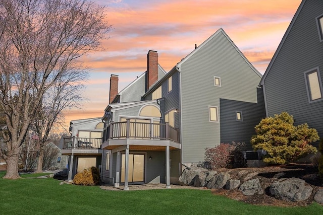 rear view of house with a chimney, a lawn, and a wooden deck