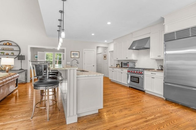29 Flat Pond Cir, Mashpee, MA 02649 - kitchen with high quality appliances, wall chimney exhaust hood, a sink, a breakfast bar, and white cabinetry