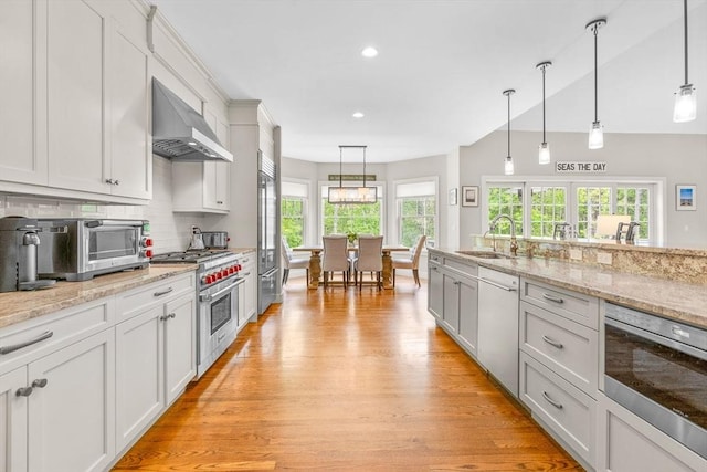 29 Flat Pond Cir, Mashpee, MA 02649 - kitchen featuring high quality appliances, wall chimney range hood, a sink, light wood-style flooring, and tasteful backsplash